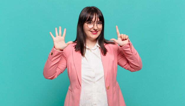 Mujer de negocios joven sonriendo y mirando amigable, mostrando el número siete o séptimo con la mano hacia adelante, contando hacia atrás