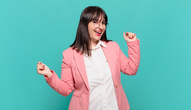 Mujer de negocios joven sonriendo, sintiéndose despreocupada, relajada y feliz, bailando y escuchando música, divirtiéndose en una fiesta