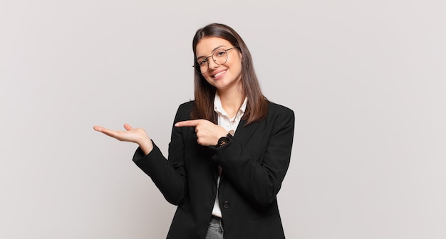 Mujer de negocios joven sonriendo, sintiéndose feliz, despreocupada y satisfecha, señalando el concepto o la idea en el espacio de la copia en el lateral