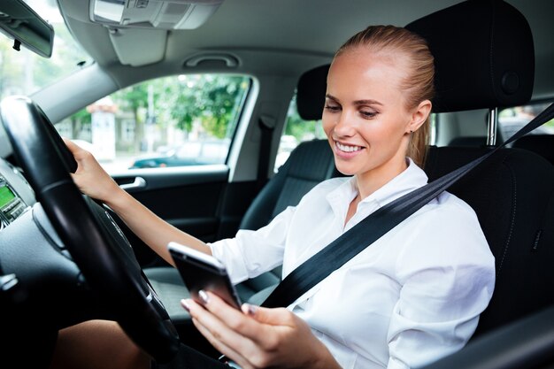 Mujer de negocios joven sonriente marcando el número de teléfono mientras conduce el coche