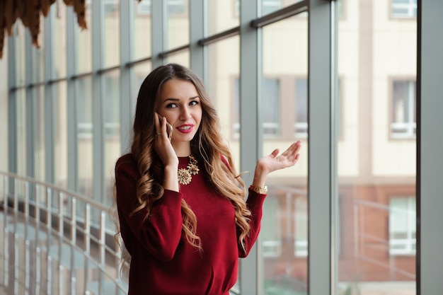 Mujer de negocios joven en un suéter rojo con teléfono móvil.