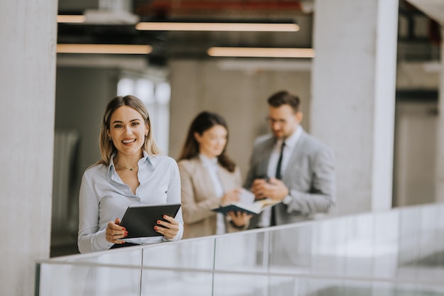 Mujer de negocios joven con tableta digital en el pasillo de la oficina