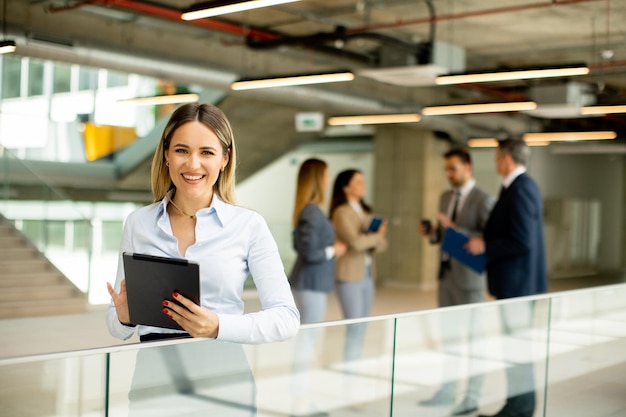 Mujer de negocios joven con tableta digital en el pasillo de la oficina