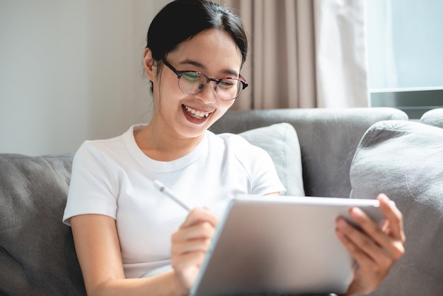 Mujer de negocios joven trabaja en casa con tableta o computadora portátil, usando tecnología de comunicación en línea, gente asiática en estilo de vida feliz, persona hermosa niña quedarse en casa