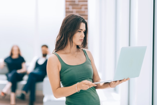 Mujer de negocios joven usa la computadora portátil mientras está de pie en la oficina .foto con espacio de copia