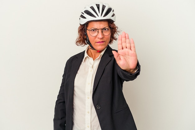 Mujer de negocios latina de mediana edad con un casco de bicicleta aislado sobre fondo blanco de pie con la mano extendida mostrando la señal de stop, impidiéndote.
