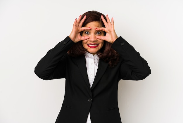 Mujer de negocios latinos de mediana edad aislada manteniendo los ojos abiertos para encontrar una oportunidad de éxito.