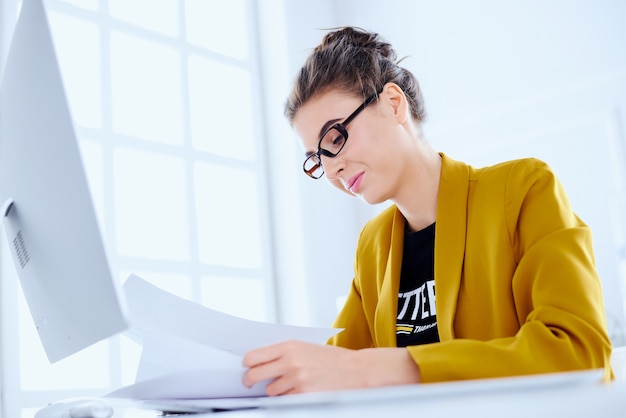 Mujer de negocios leyendo documentos y sentado en el escritorio en la oficina