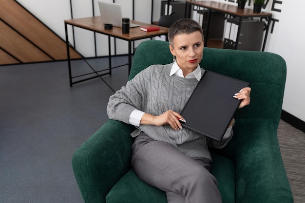 Mujer de negocios leyendo un informe en una carpeta de cuero sentada en una silla en la oficina