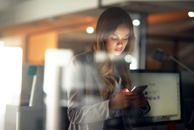 Mujer de negocios leyendo un mensaje en el teléfono revisando notificaciones y buscando un taxi en línea después de trabajar hasta tarde en la oficina oscura Empleado profesional corporativo y trabajador desplazándose en las redes sociales