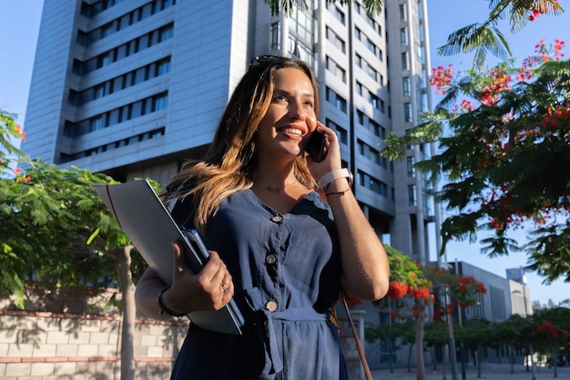 Mujer de negocios llamando con móvil en la calle con edificio de oficinas en el fondo