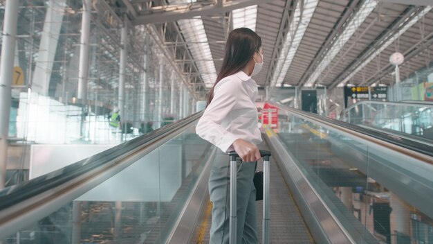 Una mujer de negocios lleva una máscara protectora en el aeropuerto internacional, viaja bajo la pandemia de Covid-19, viajes de seguridad, protocolo de distanciamiento social, nuevo concepto de viaje normal