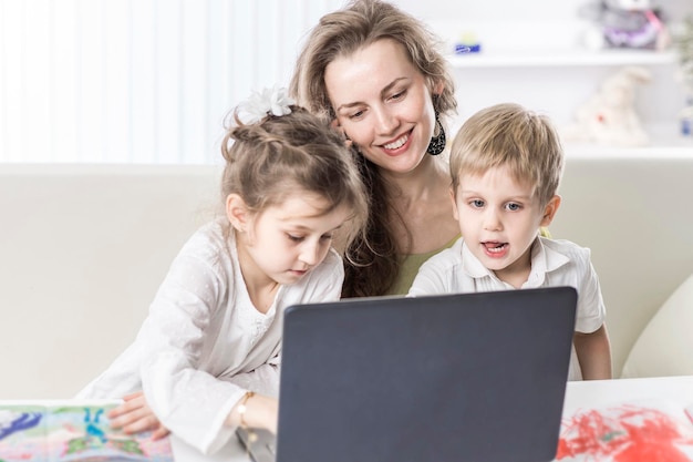 Mujer de negocios de madre joven que trabaja en una computadora portátil y habla por teléfono inteligente al lado de sus hijos