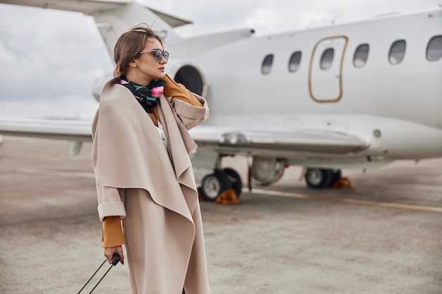 Mujer de negocios madura en abrigo cerca de su jet en el aeropuerto