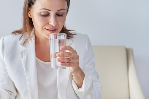 Una mujer de negocios madura bebe agua, un primer plano de la cara femenina y un vaso de agua, copia espacio. Estilo de vida saludable y comida, dieta.