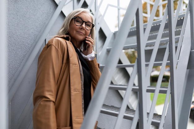 Mujer de negocios madura hablando por teléfono en las escaleras afuera