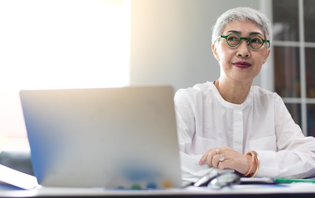 Mujer de negocios madura hermosa atractiva que trabaja en la computadora portátil en la oficina en casa moderna.