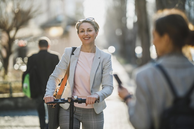 Una mujer de negocios madura montando un scooter eléctrico de camino al trabajo.