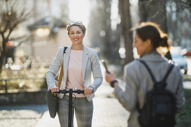 Una mujer de negocios madura va a trabajar con un scooter eléctrico.