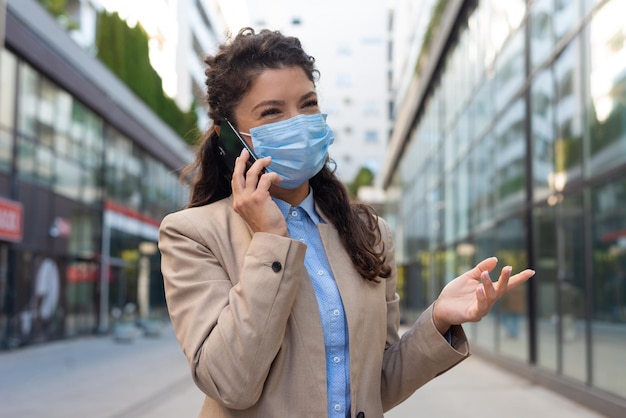 Mujer de negocios con mascarilla y hablando con alguien en su teléfono móvil mientras camina