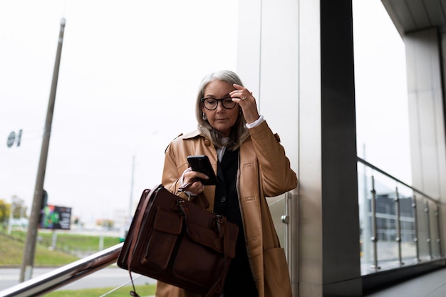 Una mujer de negocios mayor de mediana edad con un maletín y un teléfono en las manos tiene prisa por encontrarse