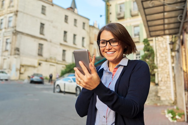 Mujer de negocios de mediana edad en gafas cardigan con teléfono móvil