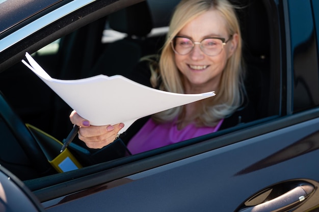 Mujer de negocios de mediana edad con gafas dando papeles a través de la ventana del coche centrándose en la mano