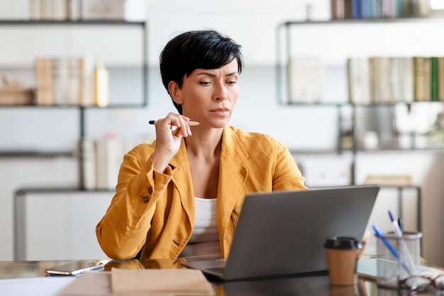 Mujer de negocios de mediana edad perdida en sus pensamientos en el lugar de trabajo cerca de la computadora portátil