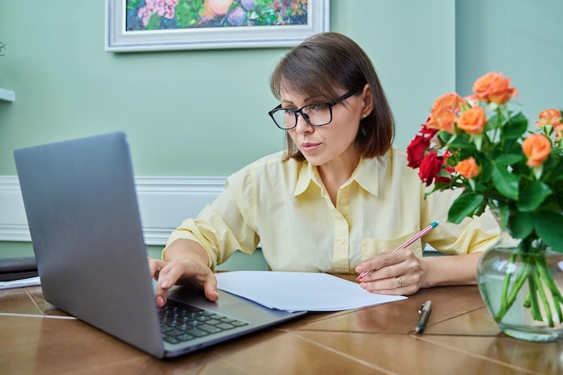 Mujer de negocios de mediana edad que trabaja desde casa en el escritorio usando una computadora portátil