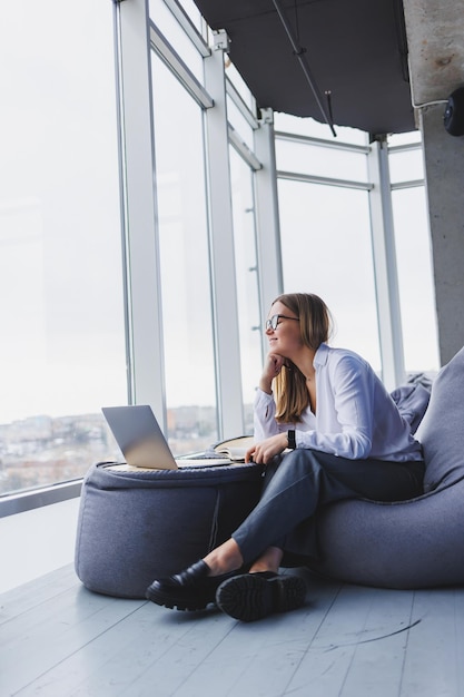 Una mujer de negocios mira la pantalla sentada en un café con una computadora portátil, toma notas en su cuaderno mirando la pantalla de la computadora portátil sentada en un café con café cerca de la ventana