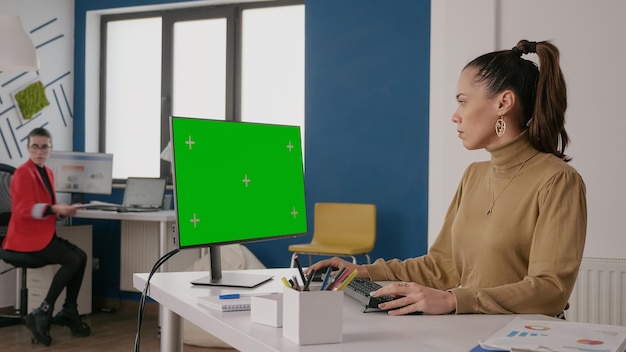 Mujer de negocios mirando la pantalla verde en la computadora, usando una plantilla aislada y una plantilla de maqueta de clave de croma en la pantalla del monitor. Empleado que trabaja con fondo de espacio de copia en blanco.