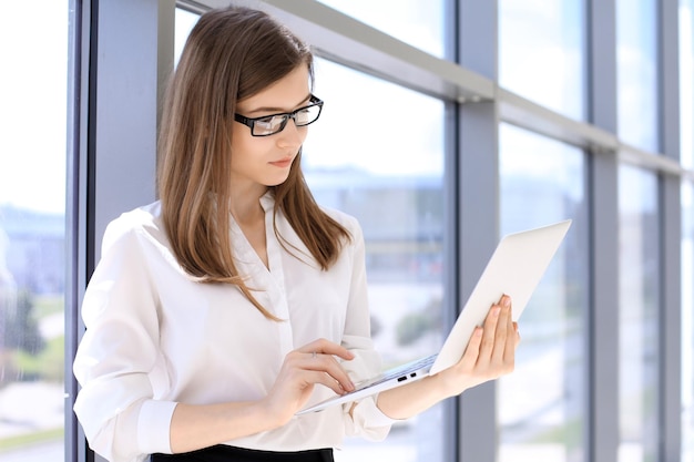 Mujer de negocios moderna escribiendo en una computadora portátil mientras está de pie en la oficina