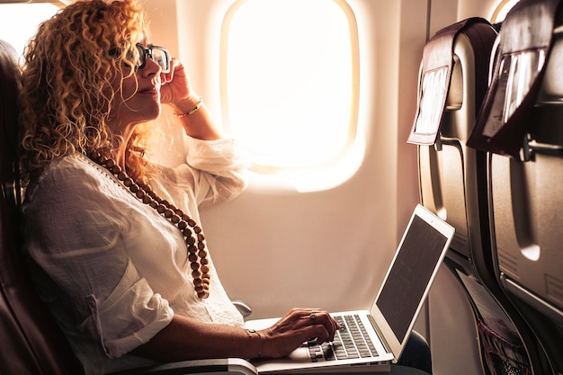 Una mujer de negocios moderna y moderna viaja sola con un avión y usa una computadora portátil con conexión inalámbrica en línea a bordo Una persona de negocios turística sentada en el asiento lista para volar Estilo de vida nómada digital