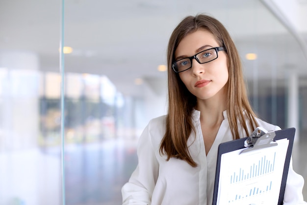 Mujer de negocios moderna de pie y guardando papeles en la oficina con espacio de copia