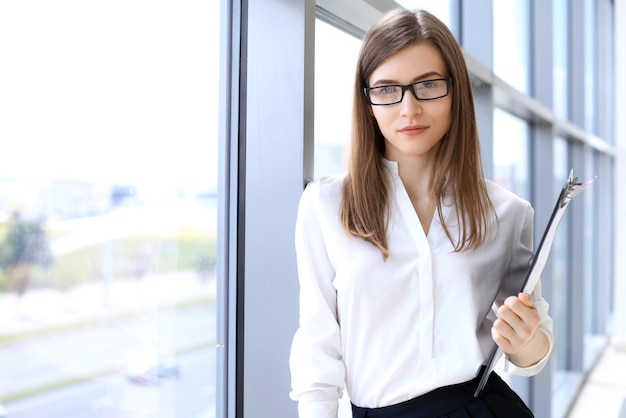 Mujer de negocios moderna de pie y manteniendo un portapapeles en la oficina