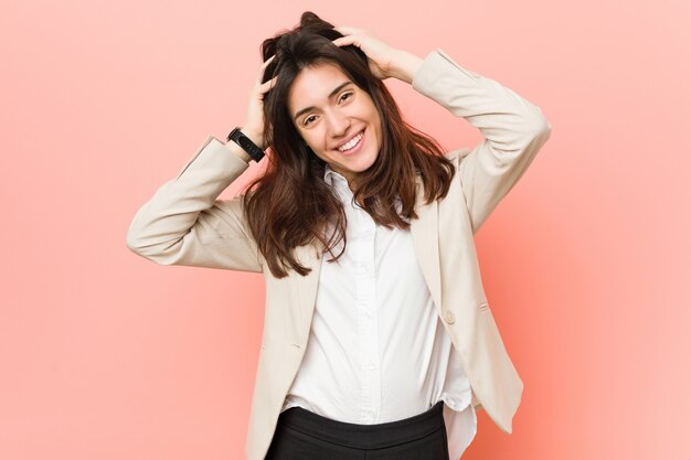 Mujer de negocios morena joven contra una rosa se ríe con alegría manteniendo las manos en la cabeza. Concepto de felicidad.