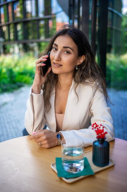 Mujer de negocios morena joven que habla en el teléfono inteligente en el café de la calle de Praga