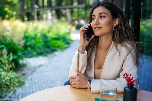 Mujer de negocios morena joven que habla en el teléfono inteligente en el café de la calle de Praga