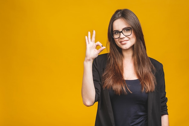 Mujer de negocios muestra símbolo ok. Retrato sonriente dentudo de la mujer de negocios aislado contra la pared amarilla.