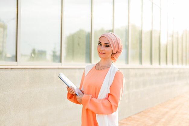 Mujer de negocios musulmana asiática joven que sonríe y que sostiene el documento de archivo al aire libre