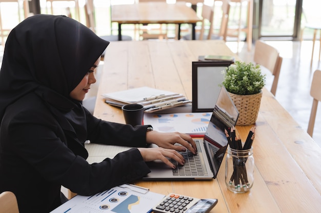 Mujer de negocios musulmana joven con hiyab negro, trabajando en coworking.
