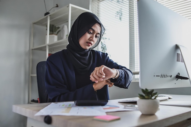 Mujer de negocios musulmana que trabaja con una computadora mientras se sienta a la mesa en una oficina y lo mira