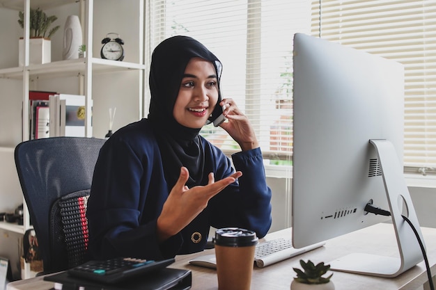 Mujer de negocios musulmana trabajando con una computadora en la oficina, teniendo una conversación de negocios en el teléfono móvil