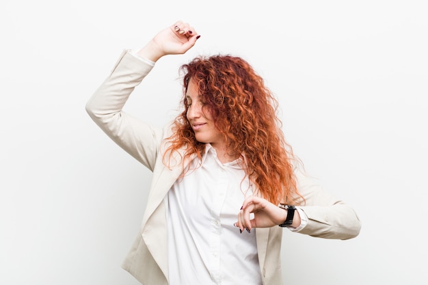 La mujer de negocios natural joven del redhead que celebra un día especial, salta y levanta los brazos con energía.