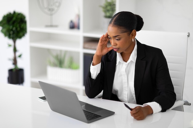 Mujer de negocios negra seria que trabaja en una computadora portátil y resuelve problemas de tareas difíciles sentado en