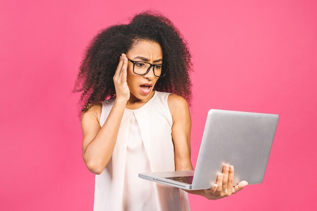 Mujer de negocios o estudiante sorprendida sorprendida, posando en rosa. Burlarse del espacio de la copia. Trabajando en una computadora portátil.