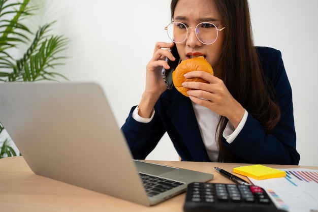 Foto mujer de negocios ocupada y cansada comiendo pan y leche para el almuerzo en la oficina de escritorio