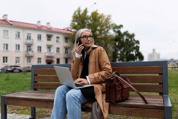 Mujer de negocios en el parque sentada en un banco hablando por un teléfono móvil trabajando en un trabajo portátil