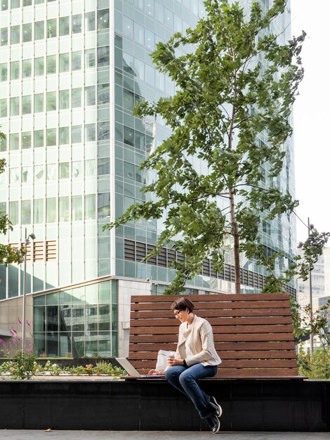 Foto mujer de negocios en un parque urbano con computadora portátil y taza de cartón de café estudiante aprende a distancia