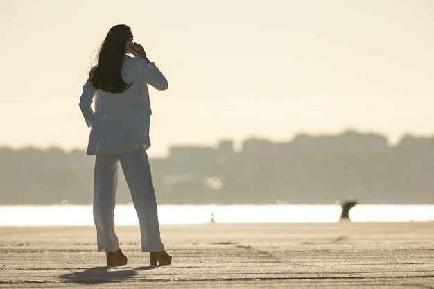 Una mujer de negocios en el paseo marítimo hablando por teléfono al atardecer